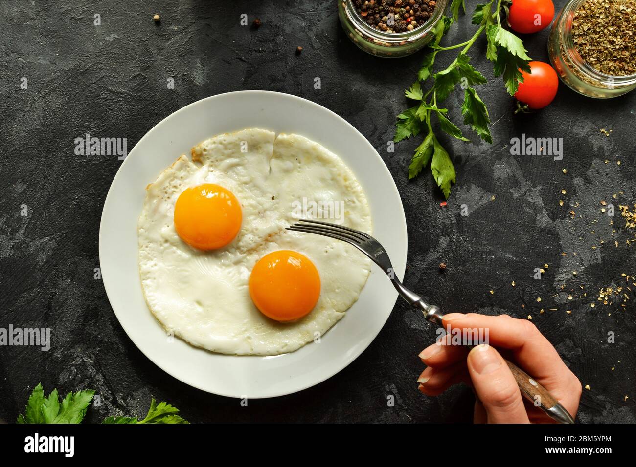 Woman eats fried eggs for breakfast, holds a fork. Fried eggs in a
