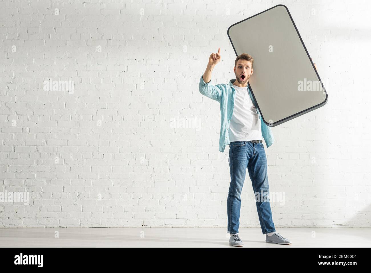 Excited man having idea while holding model of smartphone at home Stock Photo