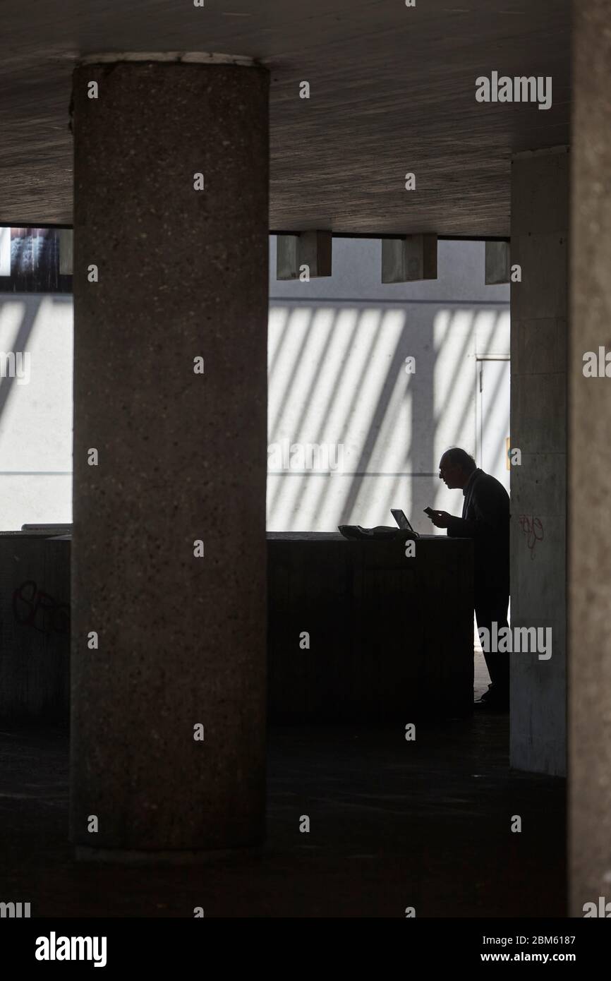 Elderly man outside Swiss Cottage library which is closed due to the Covid-19 outbreak using the WiFi internet access on his laptop, London, UK Stock Photo