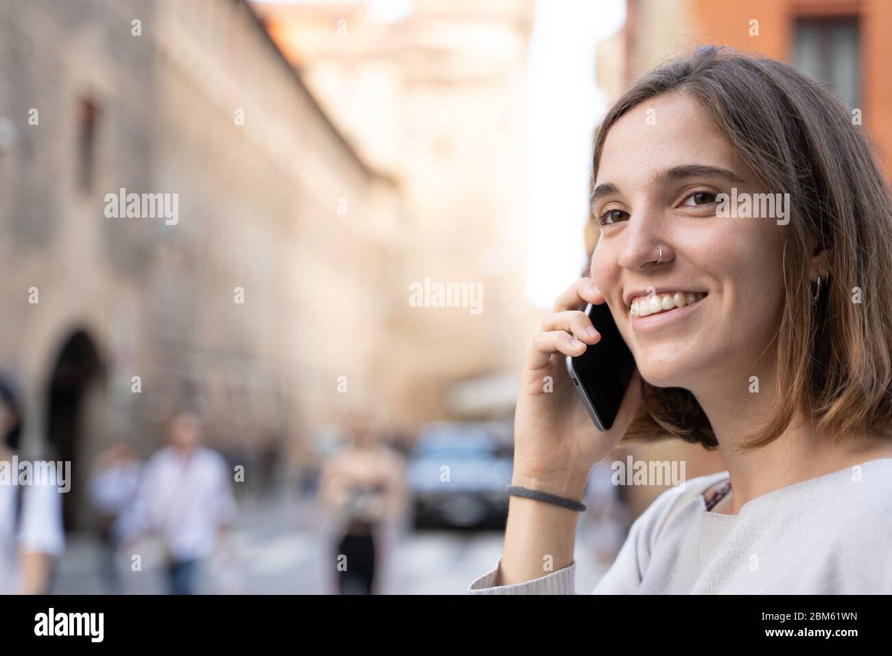 Young woman with half a mane and a pierced nose smiling and talking to her cell phone on the street Stock Photo