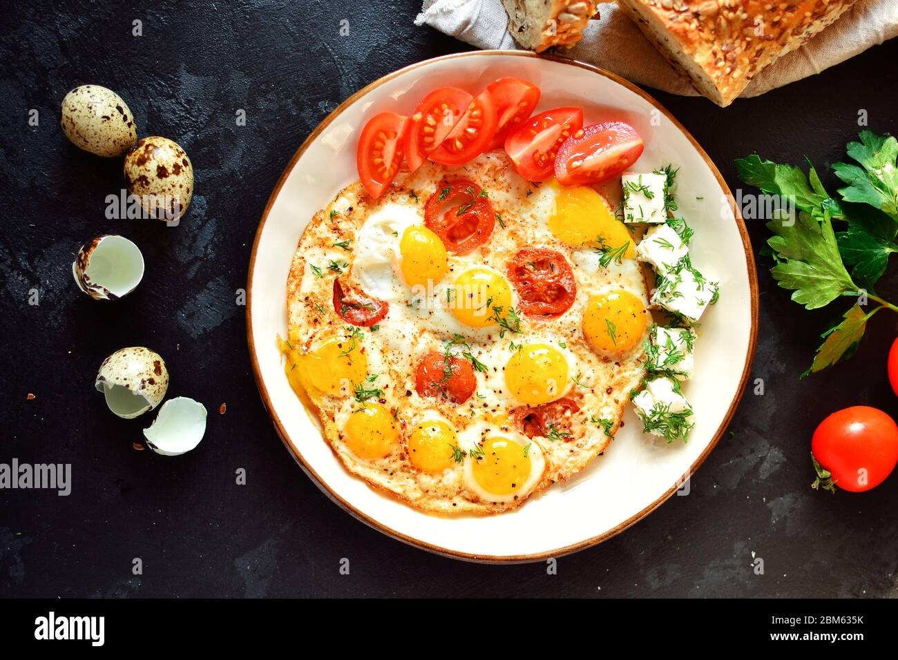 Fried quail eggs in a beautiful plate on a dark table background. Fried eggs with tomatoes and dill. Tasty and healthy breakfast. Top view Stock Photo