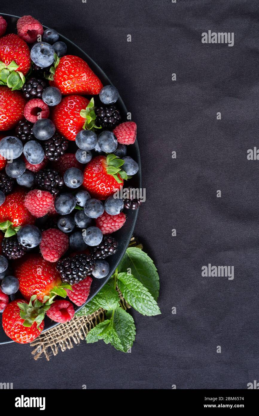 Strawberries, blackberries, rasberries, green mint on canvas black bakground. Mock up, menu, cafe poster concept Stock Photo