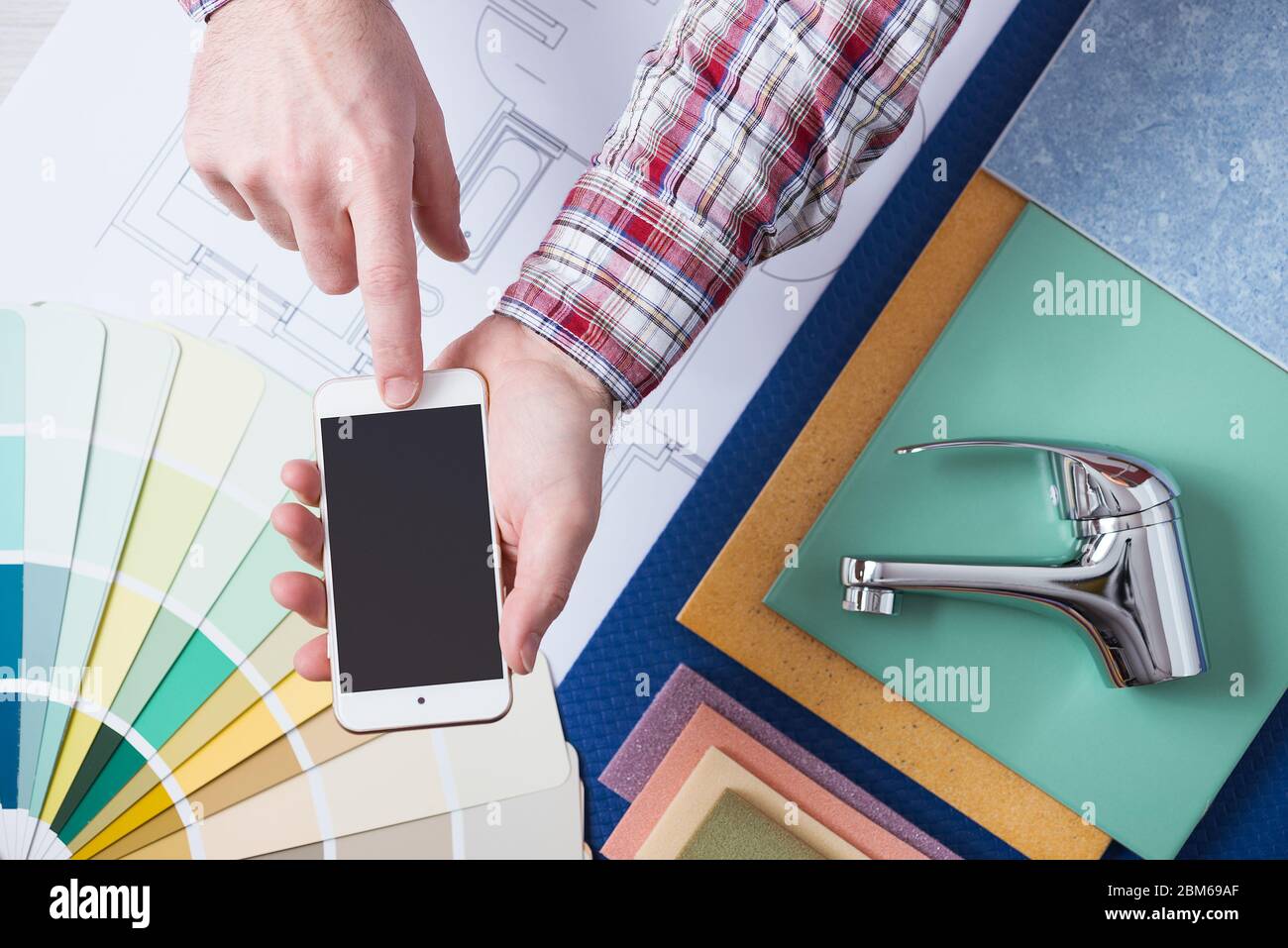 Male hands using a smart phone next to a faucet and tiles, plumber online booking and home service Stock Photo