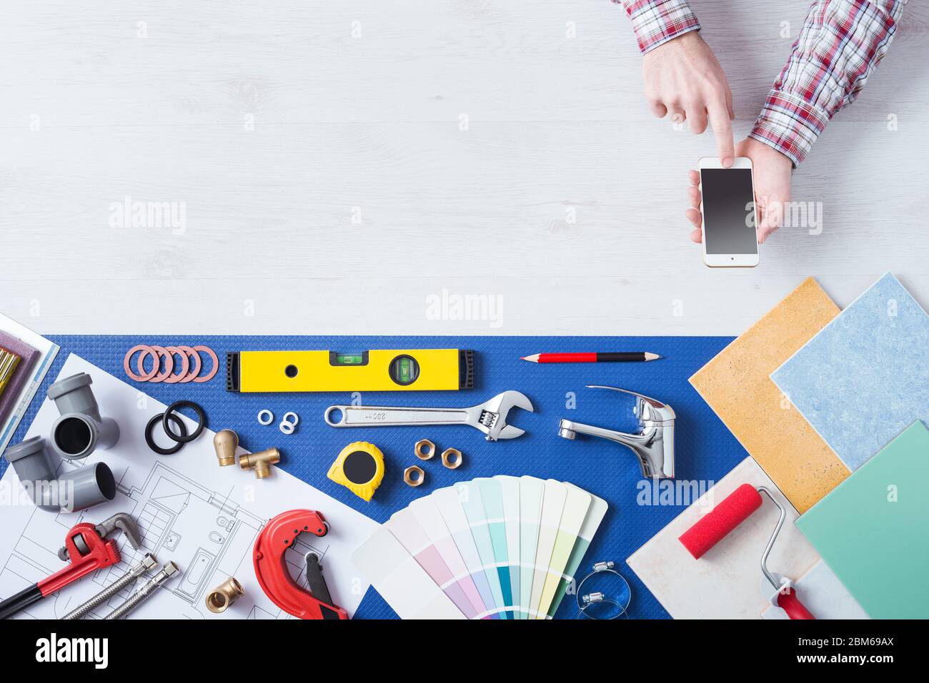 Male hands using a mobile phone next to plumbing work tools, tiles and swatches, online booking and home plumbing service Stock Photo