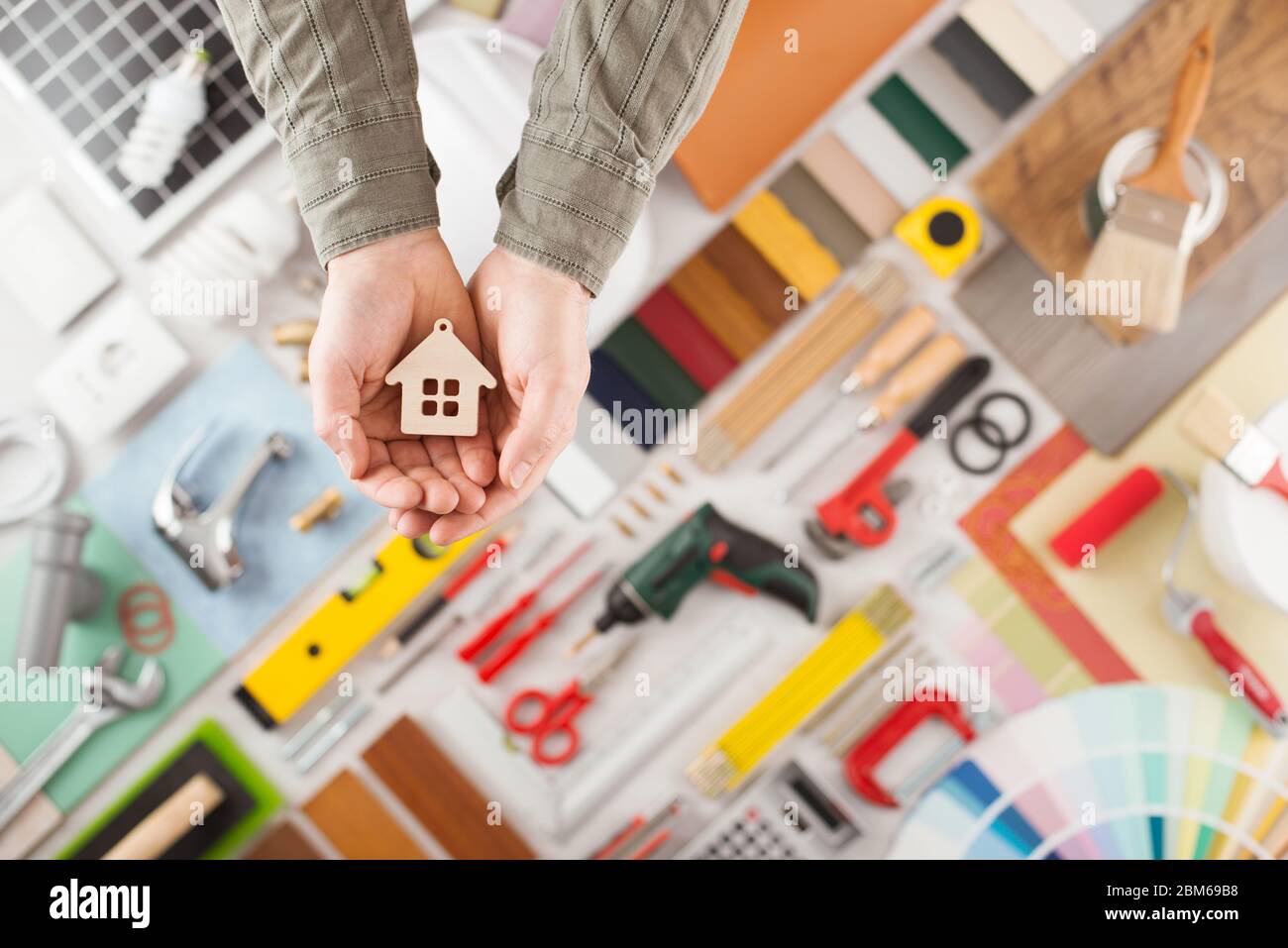 Male hands holding a small house, build and renovation tools on background top view, home insurance concept Stock Photo