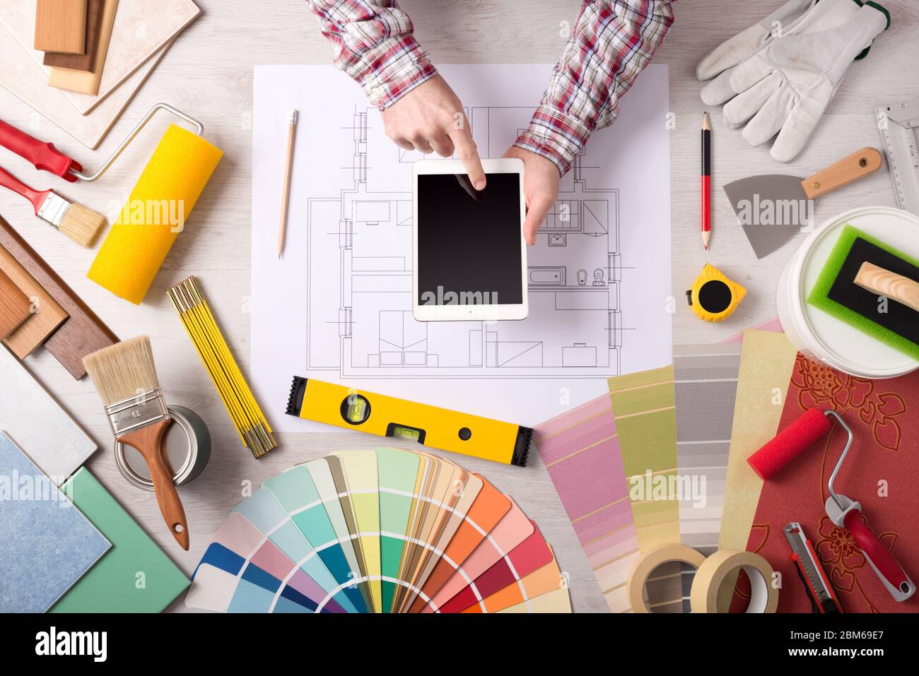 Professional decorator using a digital tablet, work tools, painting rollers and color swatches all around, top view Stock Photo