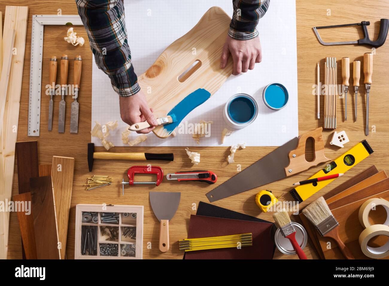 Decorator varnishing a wooden stool with a blue coating on a work table with DIY tools all around, top view Stock Photo