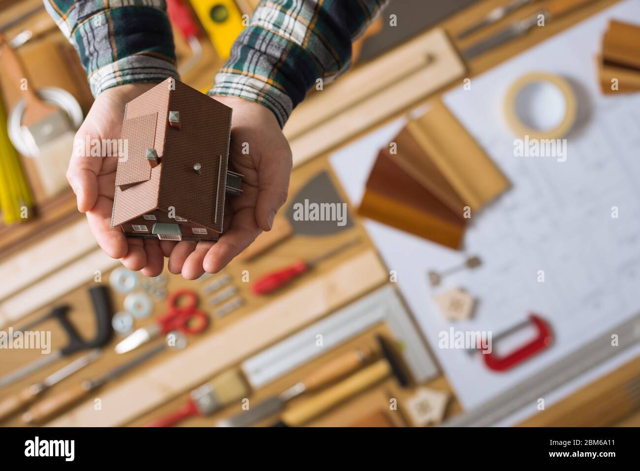 Hands holding a model house, work table with tools and blueprint project on background top view, home insurance concept Stock Photo