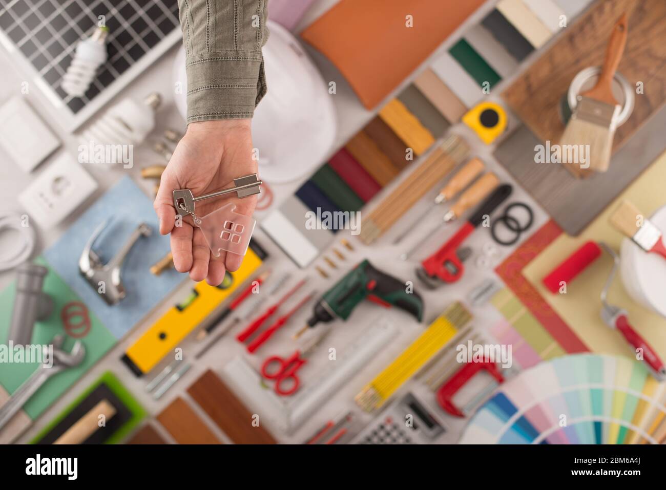 Male hand handing house keys, build and renovation tools on background, top view Stock Photo