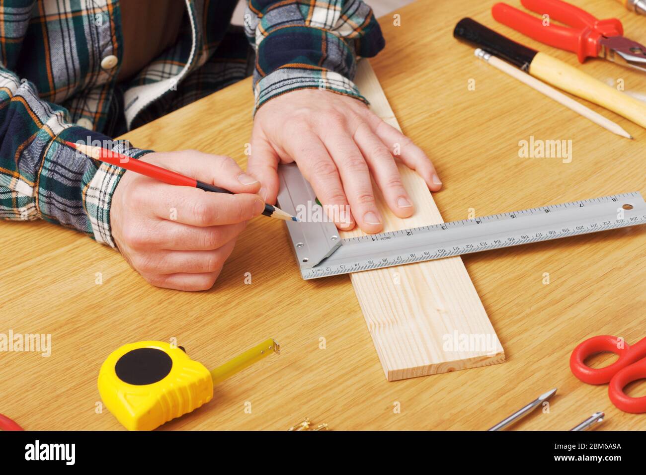 Man working on a DIY project and measuring a wooden plank with work tools all around, hands close up Stock Photo