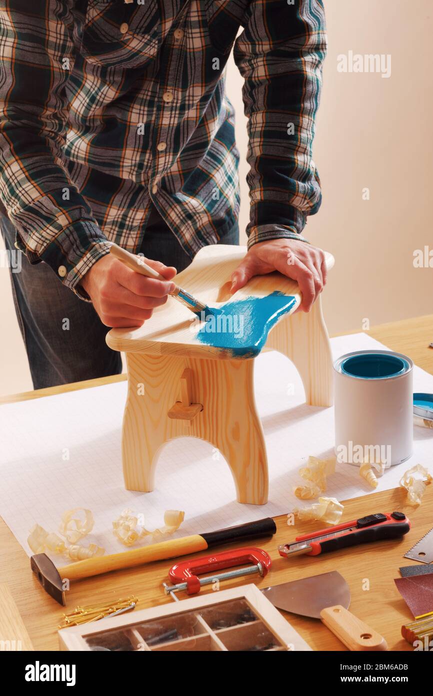 Craftsman varnishing a wooden handmade stool at home with a blue coating on a work table Stock Photo