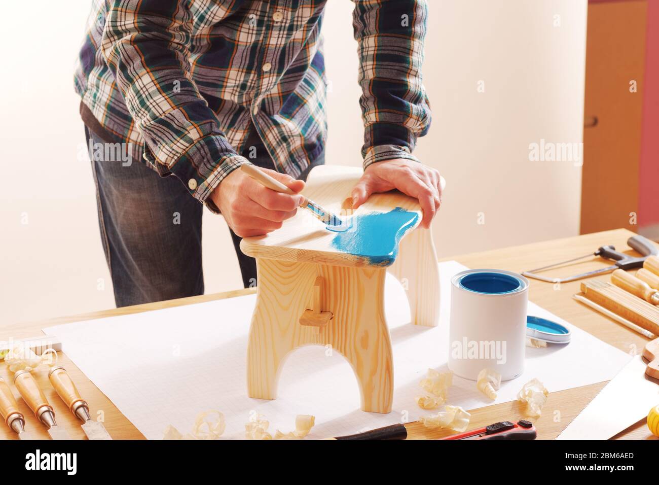 Craftsman varnishing a wooden handmade stool at home with a blue coating on a work table Stock Photo