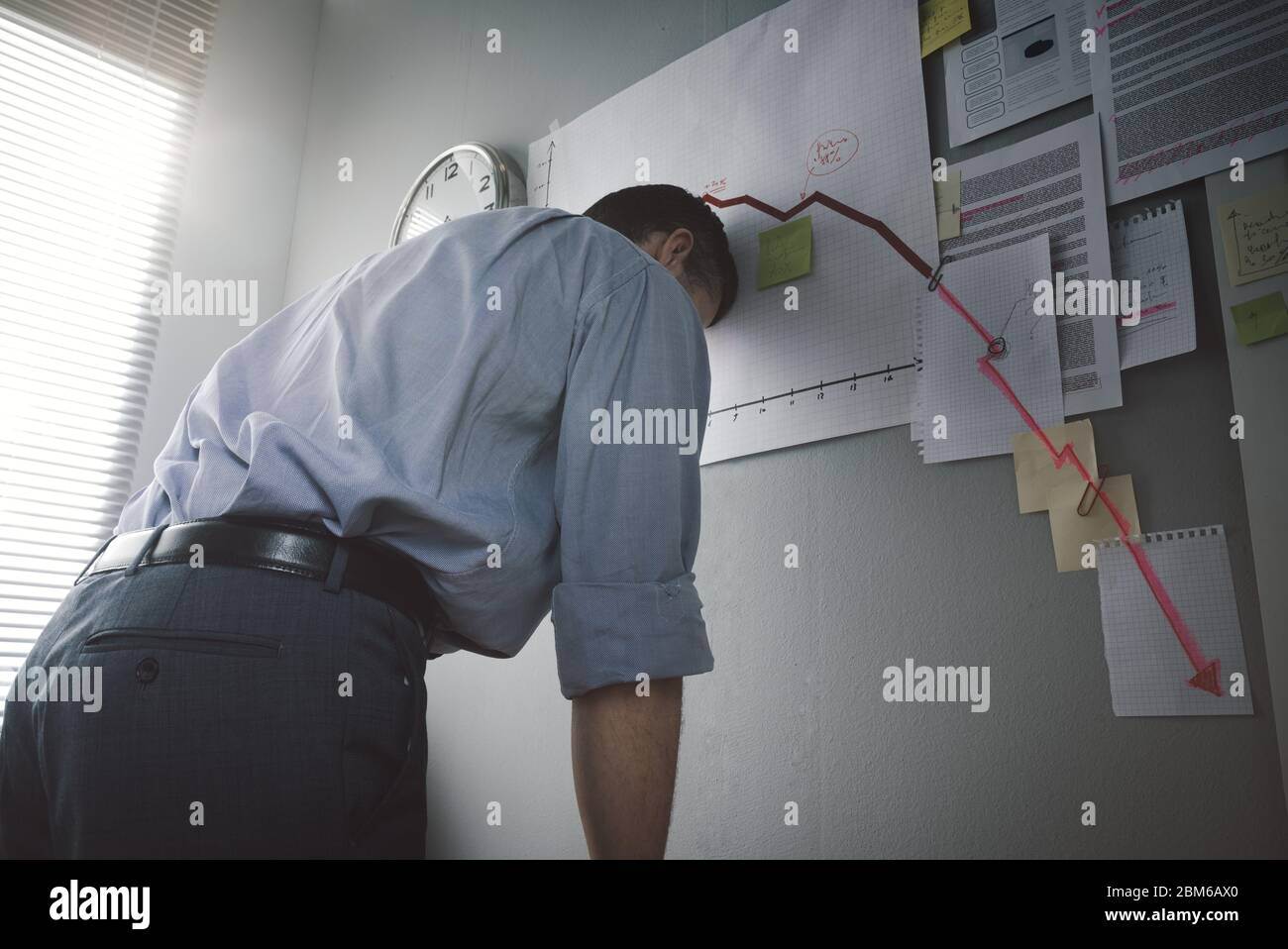 Desperate businessman with head down against a wall and financial chart with arrow going downwards. Stock Photo