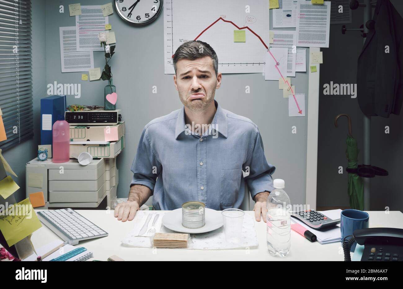 Sad businessman having lunch with canned food and negative business chart on background. Stock Photo