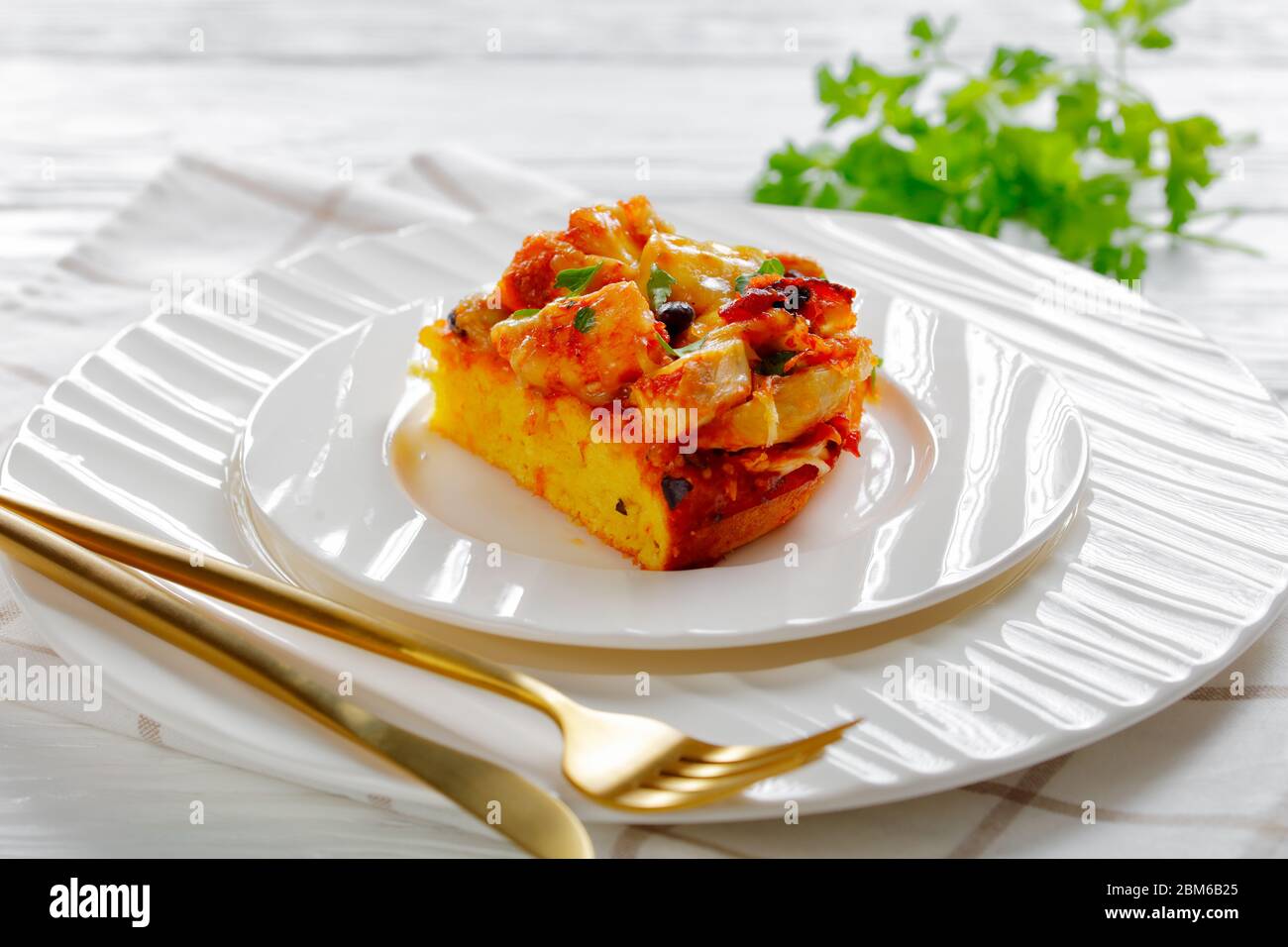 Restaurant serving of chicken tamale pie with a cornmeal mix crust, cheddar cheese, black beans served on a plate with cutlery served with sour cream Stock Photo