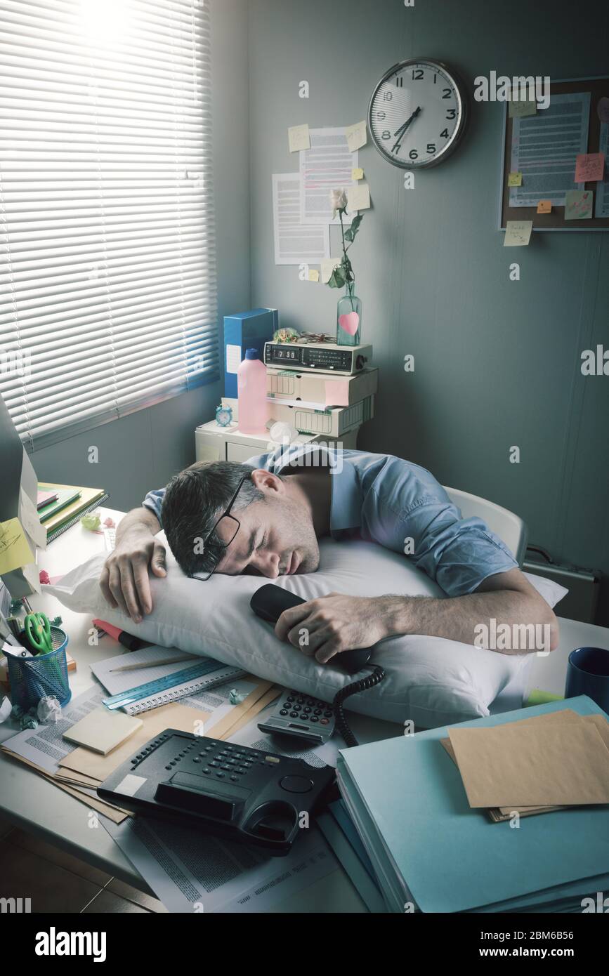 Exhausted businessman sleeping at workplace with a pillow on his desk. Stock Photo