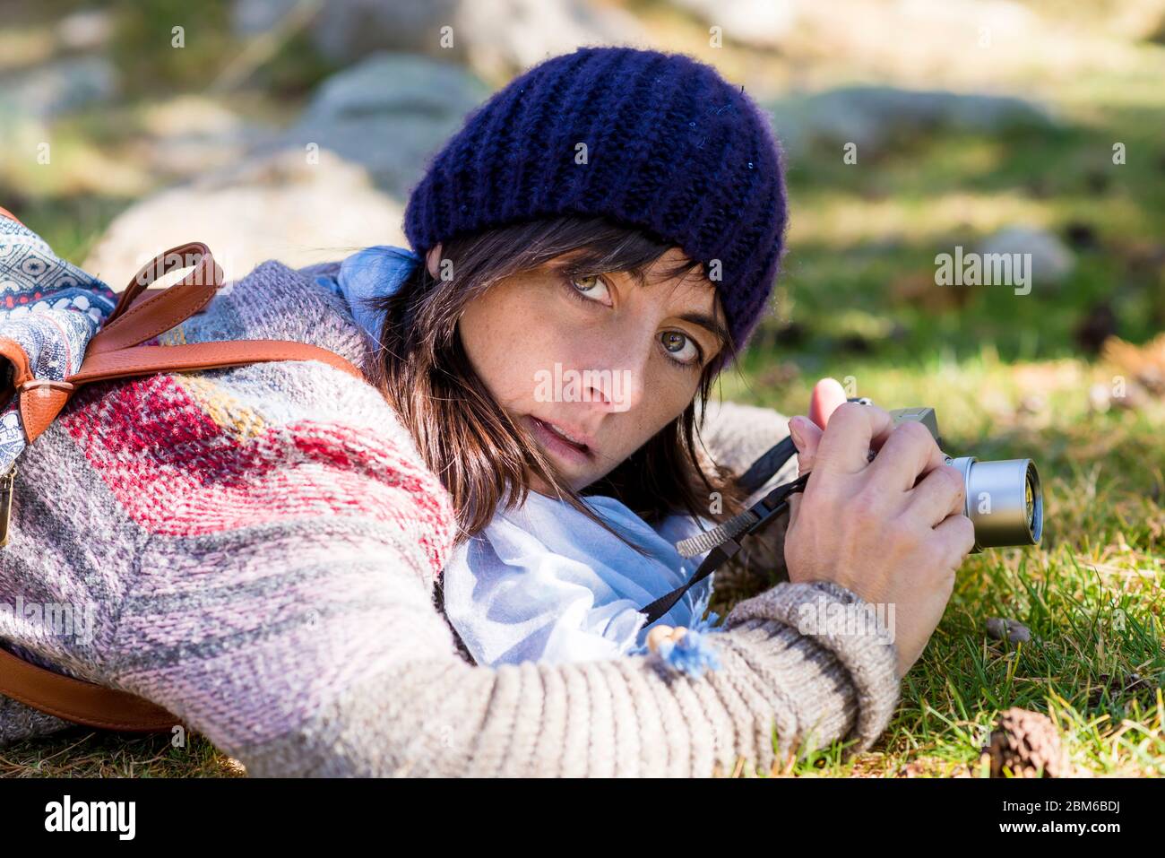 Woman with wool cap lying on the forest ground while using a camera to ...