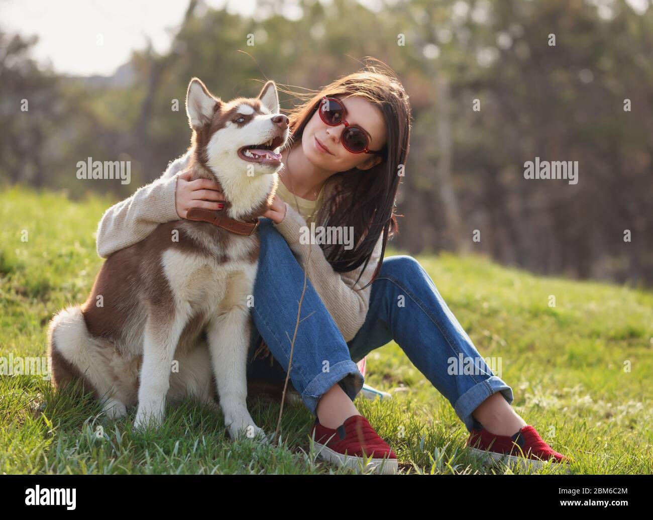 Smiling young brunette girl sitting with her husky dog in green park  outdoors. Cute and friendly couple enjoying the nature. Pretty female and  fluffy Stock Photo - Alamy