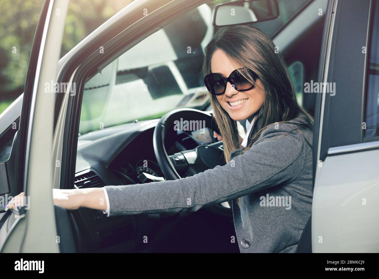 Young attractive woman opening car door after parking and smiling at camera. Stock Photo