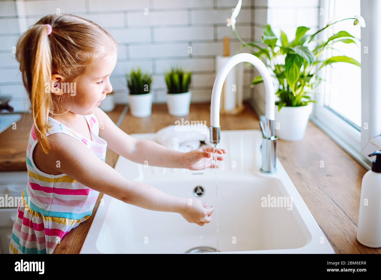 Blonde toddler girl washing hands in the light kitchen before eating. Hygiene and healthcare concept Stock Photo