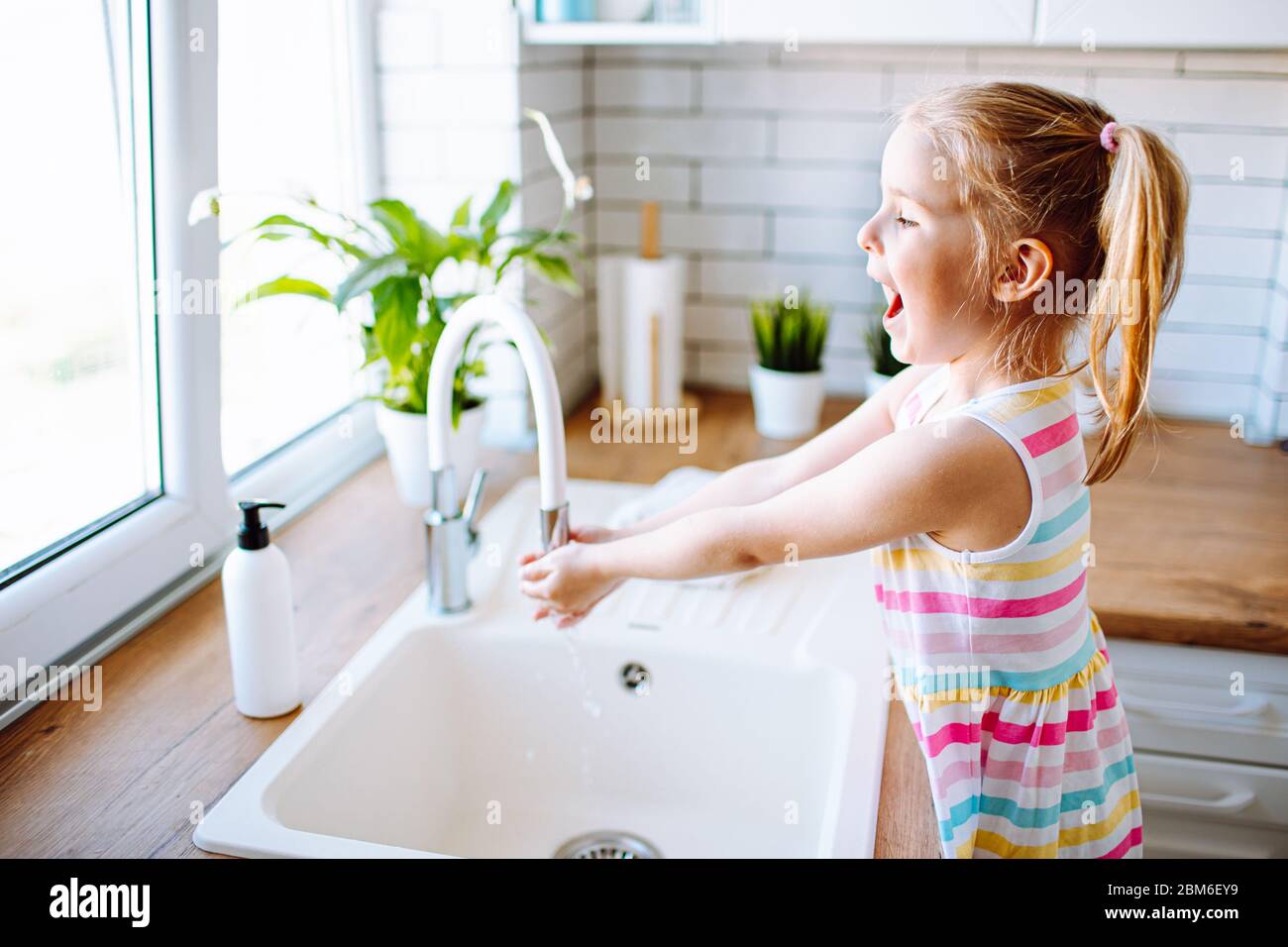 Blonde toddler girl washing hands in the light kitchen before eating
