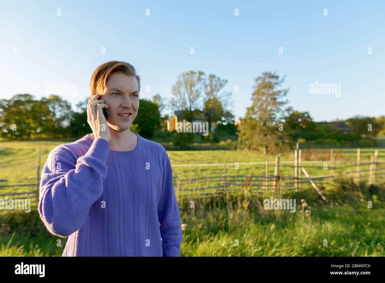 Happy young man talking on mobile phone in peaceful grassy plain with nature Stock Photo