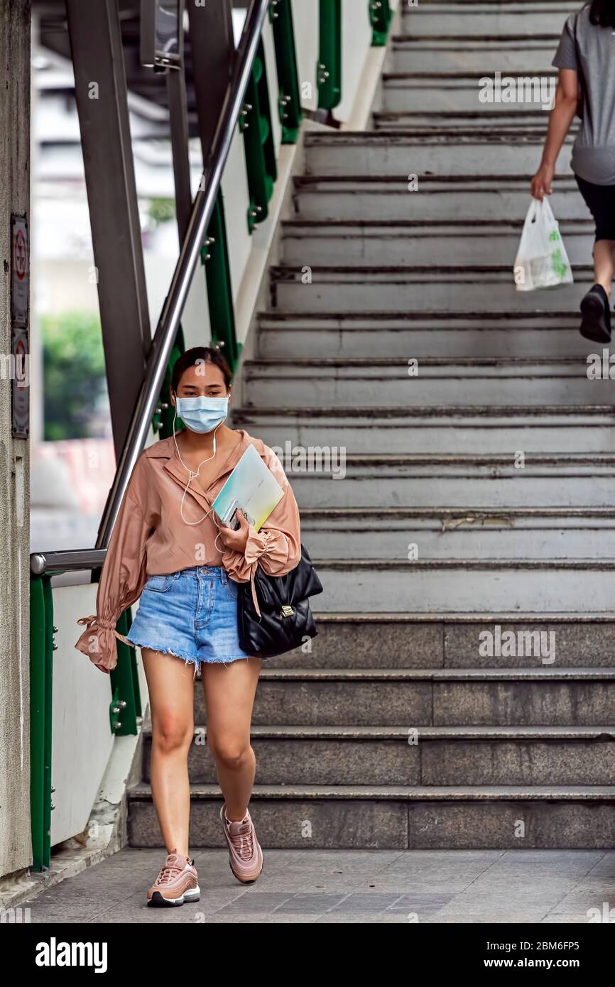 Girl with facemask walking down stairs during Covid 19 pandemic, Bangkok, Thailand Stock Photo
