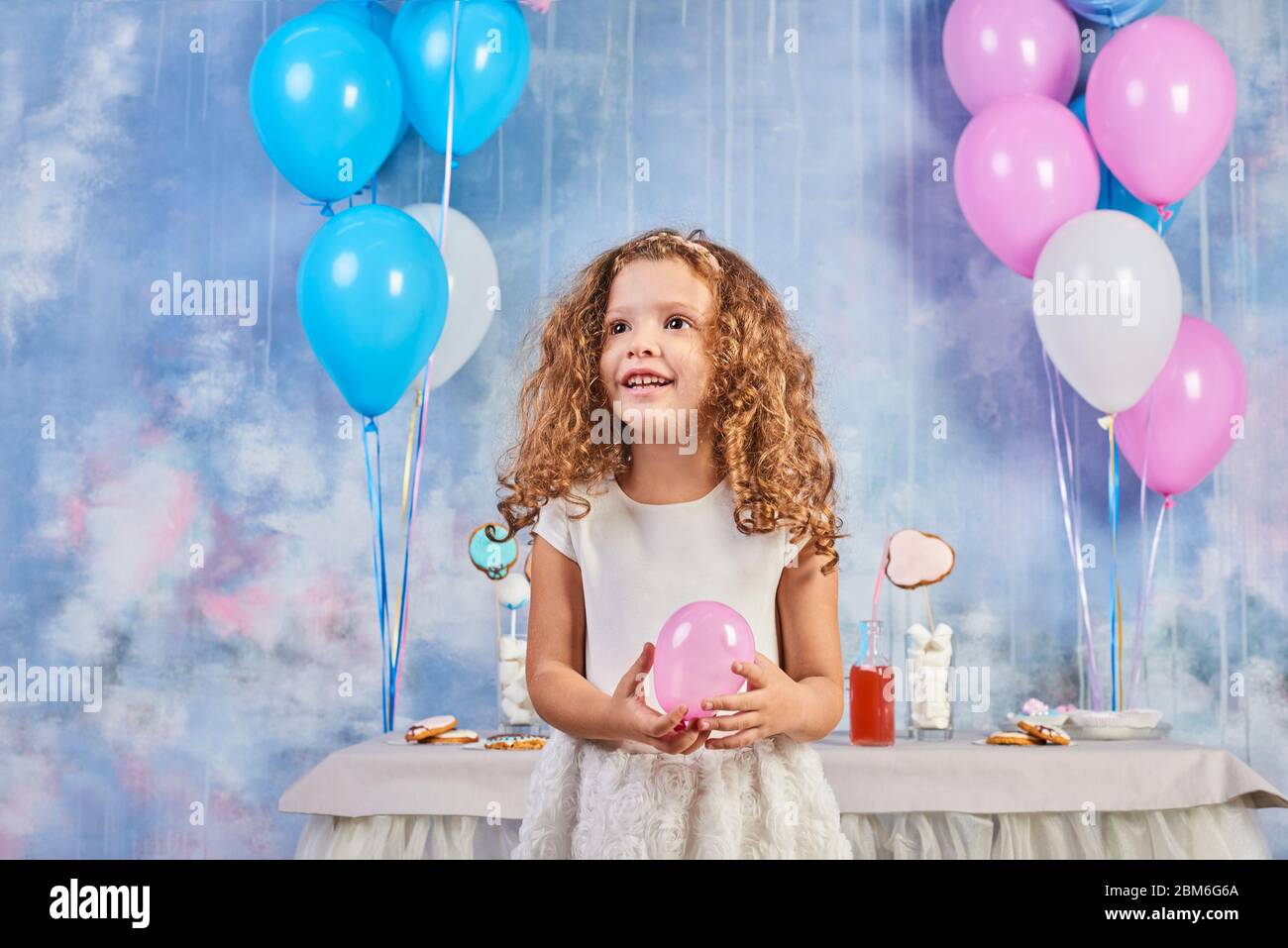 Children's funny birthday party in decorated room. Happy little girl celebrate International Children's Day. Funny child play at home Stock Photo