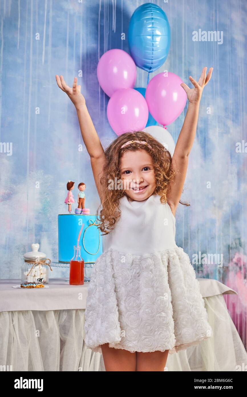 Children's funny birthday party in decorated room with balloons. Happy little girl celebrate International Children's Day. Funny child play at home Stock Photo