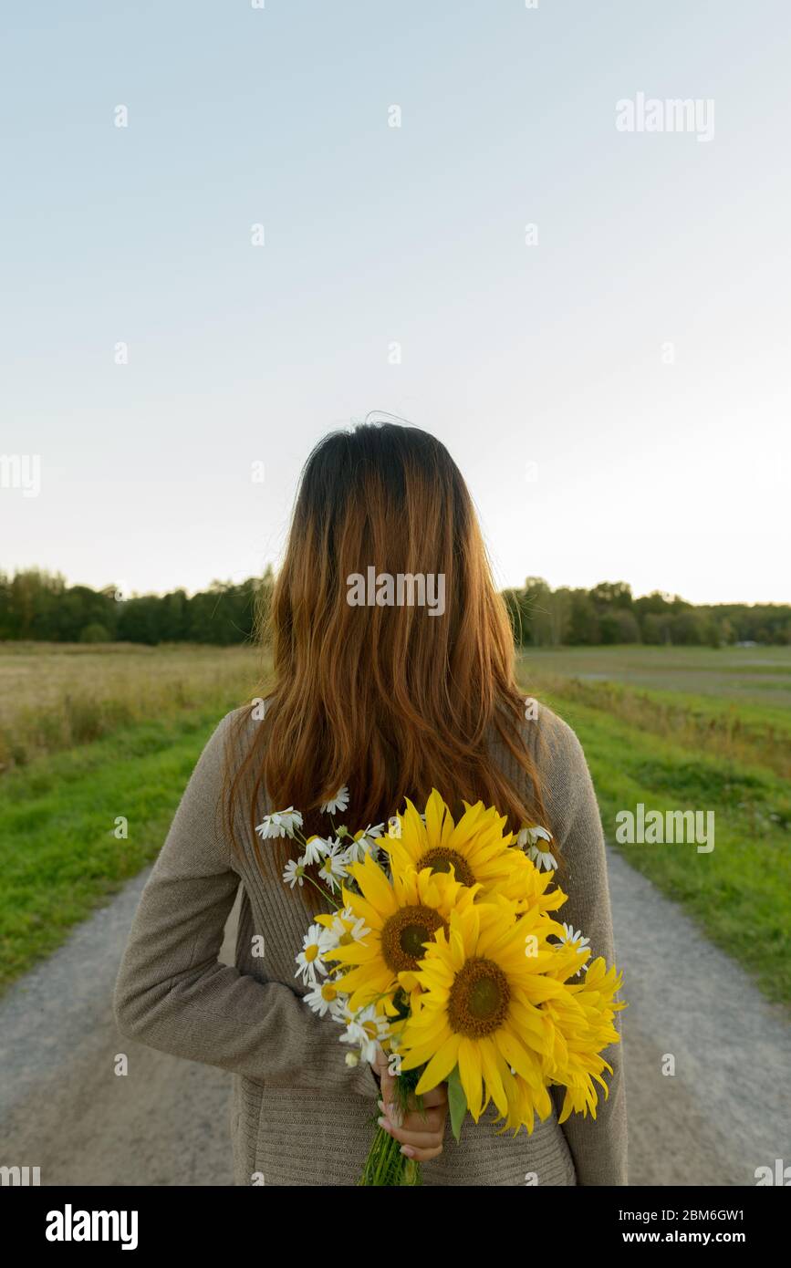 Rear view of young Asian woman holding sunflowers behind back in nature Stock Photo