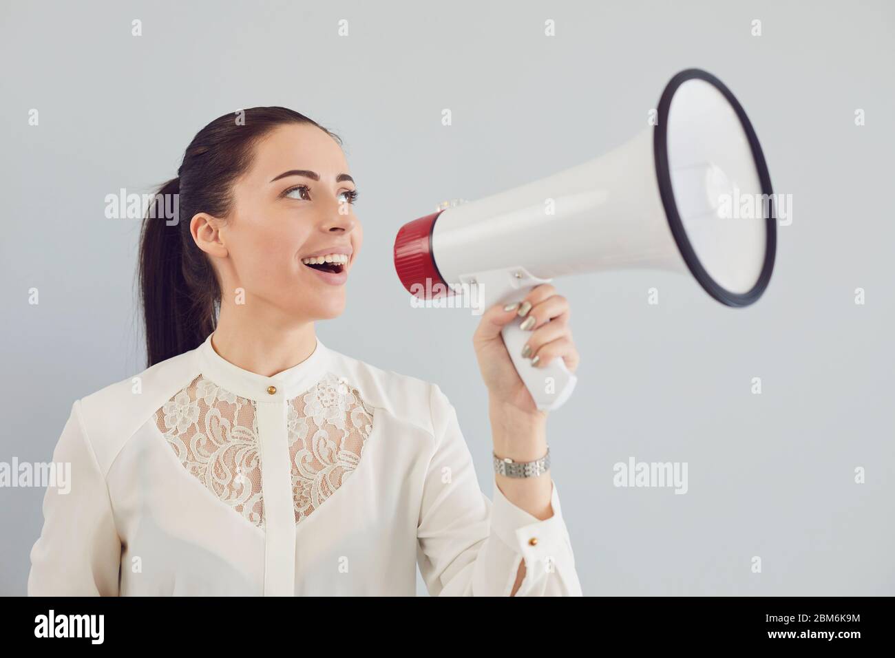 A woman in a white shirt in a bullhorn on a gray background. Stock Photo