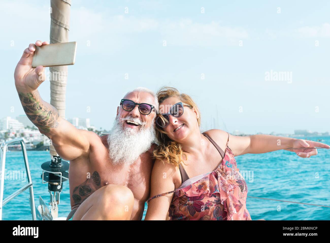 Senior couple taking selfie with mobile smartphone on sailboat vacation - Happy mature people having fun celebrating wedding anniversary on boat trip Stock Photo