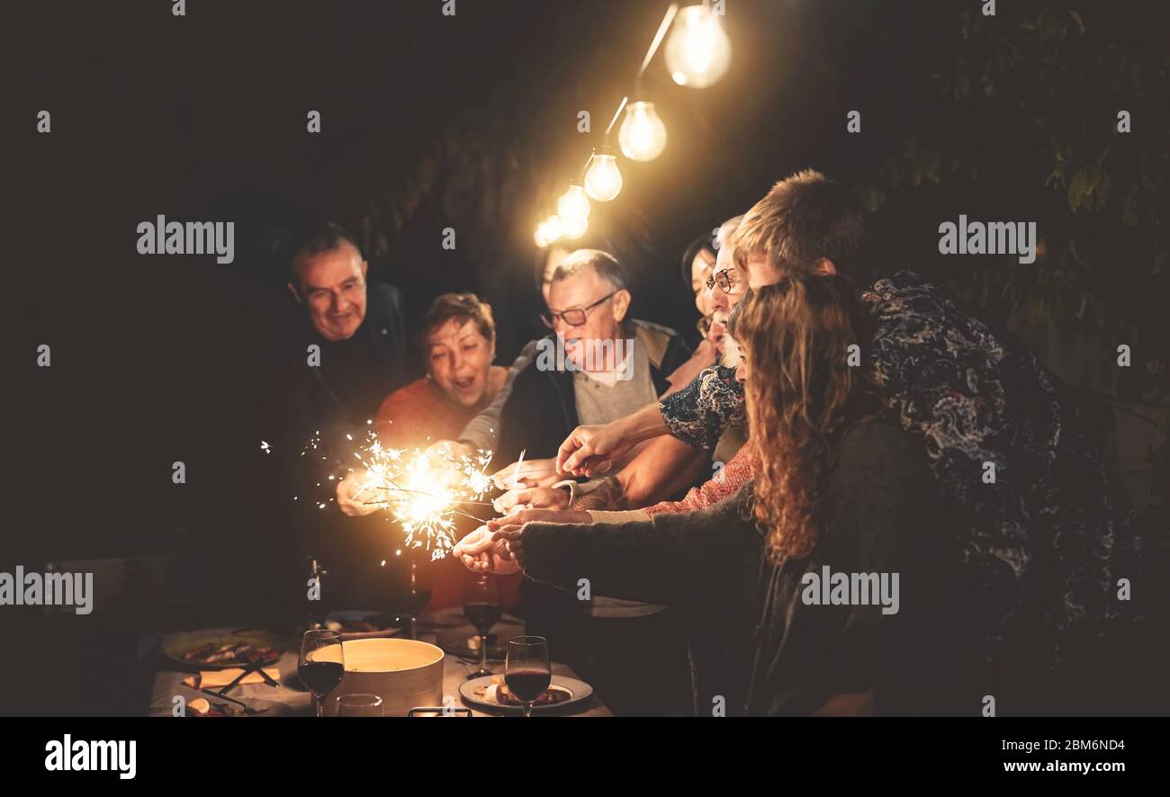 Happy family having fun at dinner night party outdoor - Group of people mixed ages celebrating together with fireworks sparklers outside Stock Photo