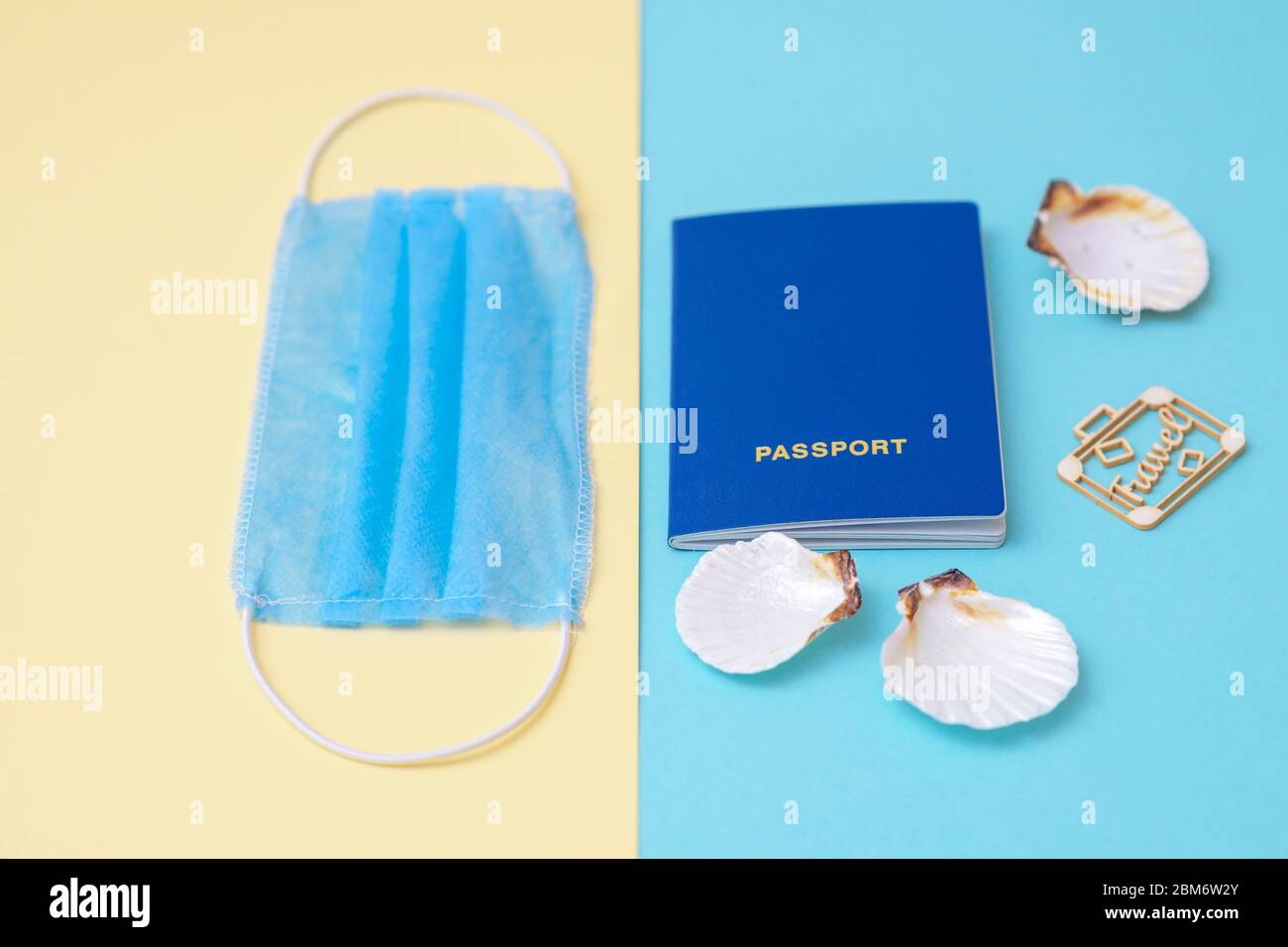 Travel concept during coronavirus. Travel and flight still life concept with a passport, medical mask and seashells on a blue and yellow background. Selective focus. Stock Photo