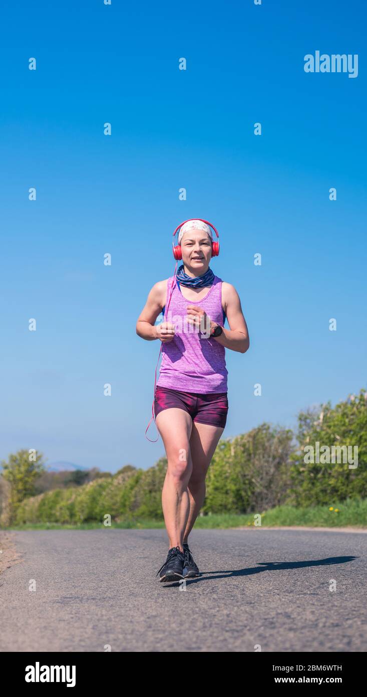 A young woman running on a country road on a sunny day dressed in black  jogging shoes, dark pink shorts and purple tshirt Stock Photo - Alamy