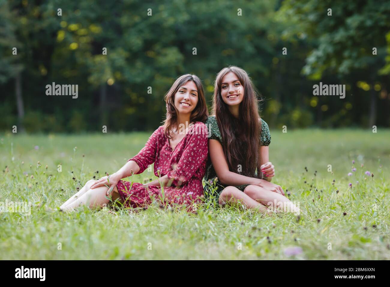 Two young smiling women sitting on grass in the park Stock Photo - Alamy