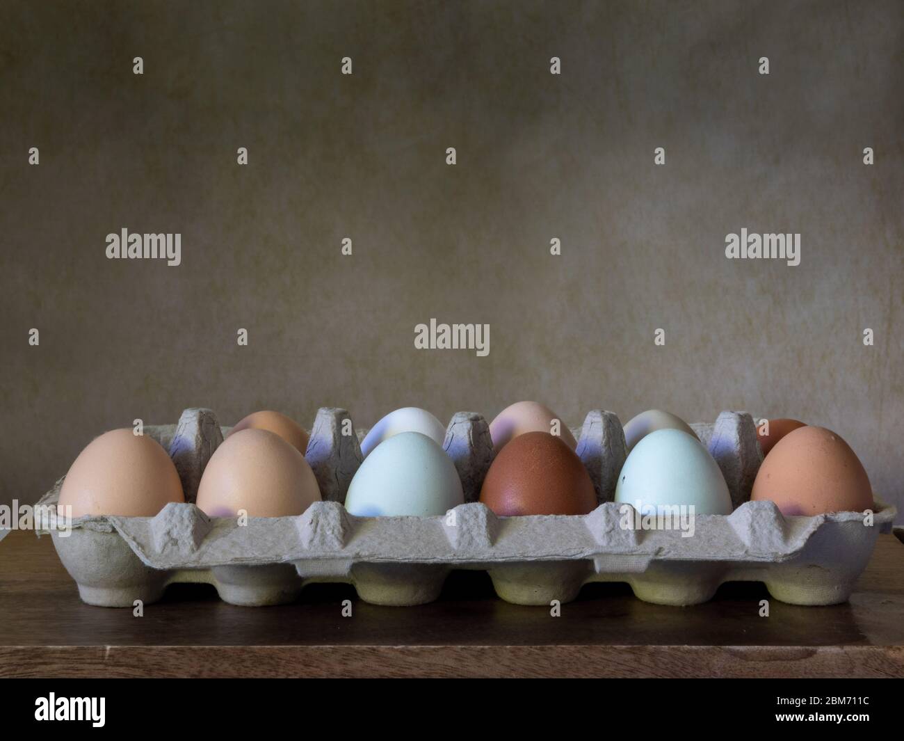 One dozen unwashed colorful chicken eggs in open cartonon on wooden