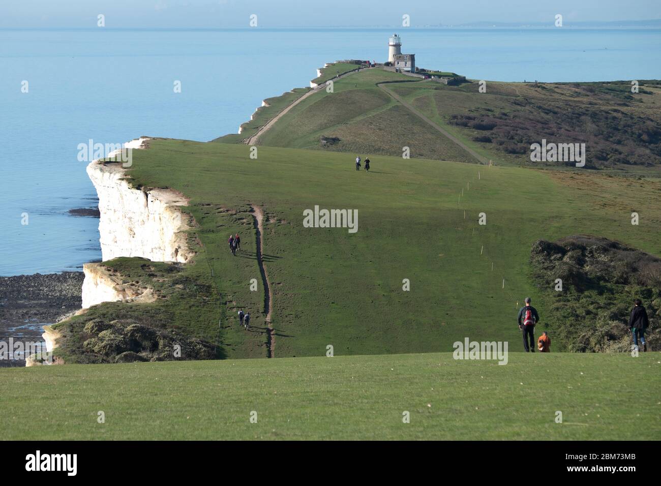 Walkers near Beachy Head on the undulating South Downs Way in East Sussex, approaching the cliff-top Belle Tout Lighthouse Stock Photo