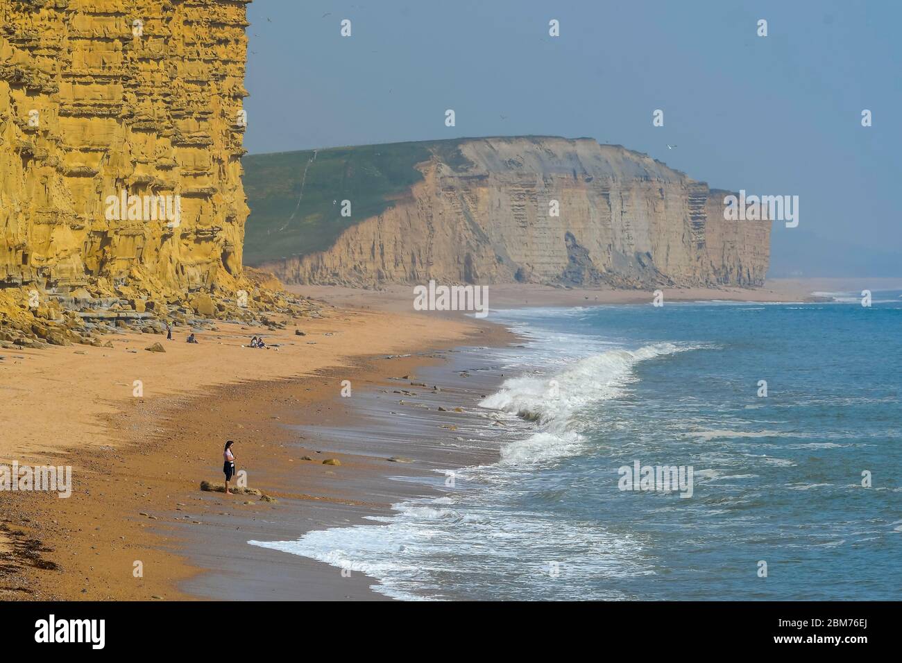West Bay, Dorset, UK.  7th May 2020. UK Weather.  A woman standing on the beach looking out to sea at the seaside resort of West Bay in Dorset enjoying the hot sunshine during the coronavirus pandemic lockdown.   Picture Credit: Graham Hunt/Alamy Live News Stock Photo