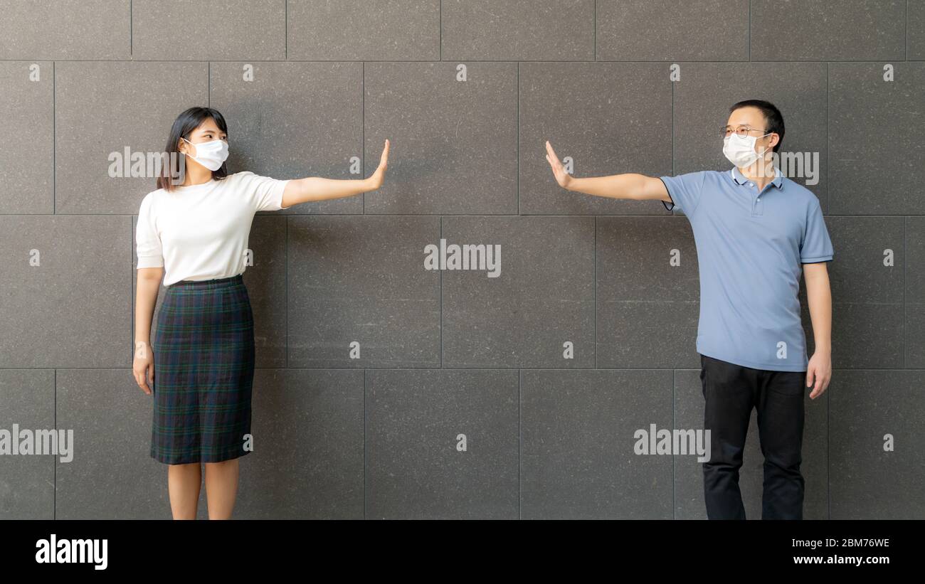 Young Asian couple wearing face masks meeting and standing against the wall in outdoors for social distancing for infection risk and disease preventio Stock Photo