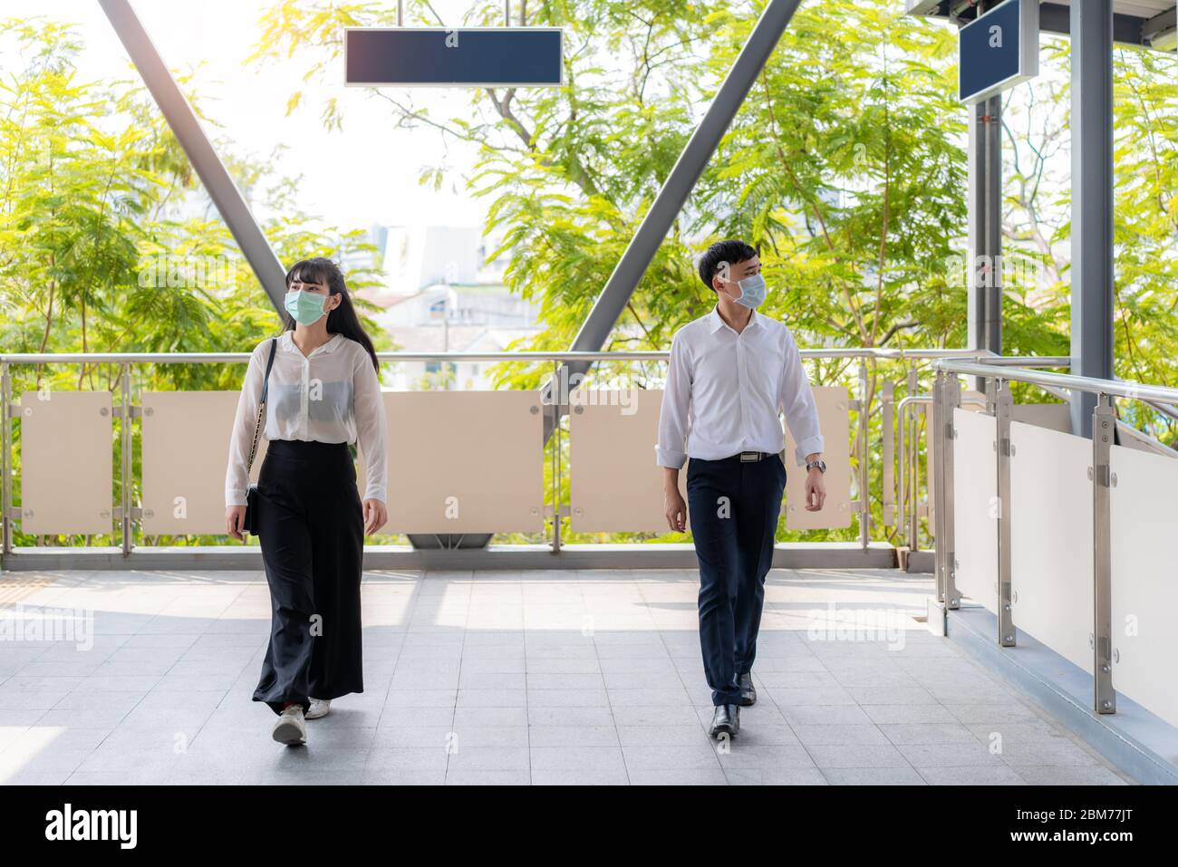 Two Asian man and woman keep distance of two meters or 6 feet between each person walking on footpath or skywalk for social distancing for infection r Stock Photo