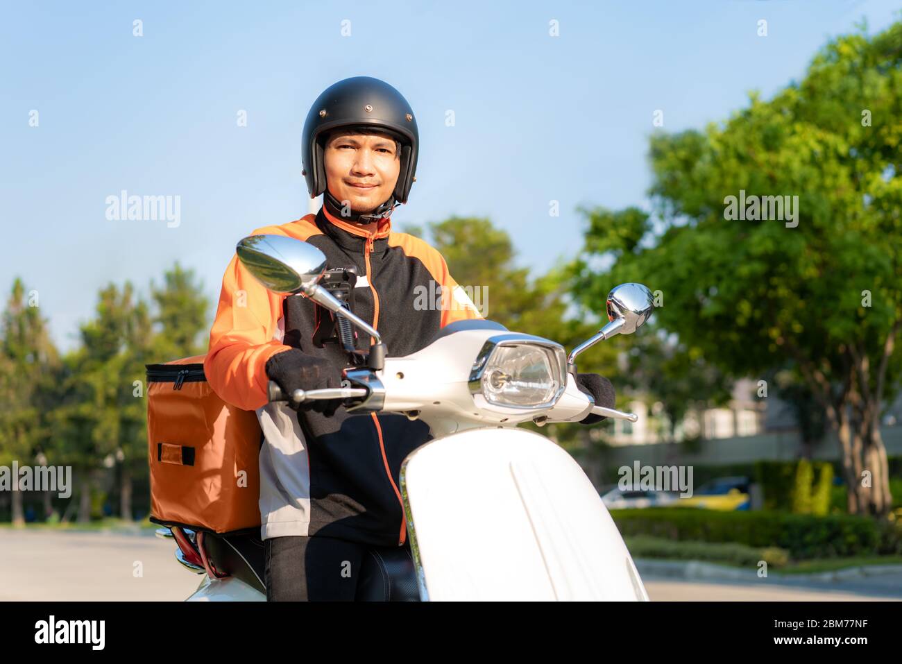 Asian man courier on scooter delivering food in town streets with a hot food delivery from take aways and restaurants to home, express food delivery a Stock Photo