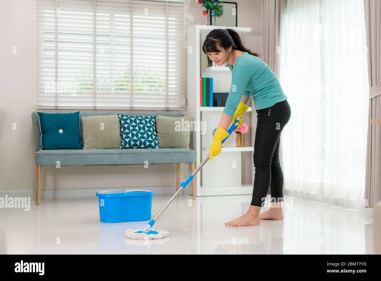 Attractive young Asian woman mopping tile floor at living room while doing cleaning at home