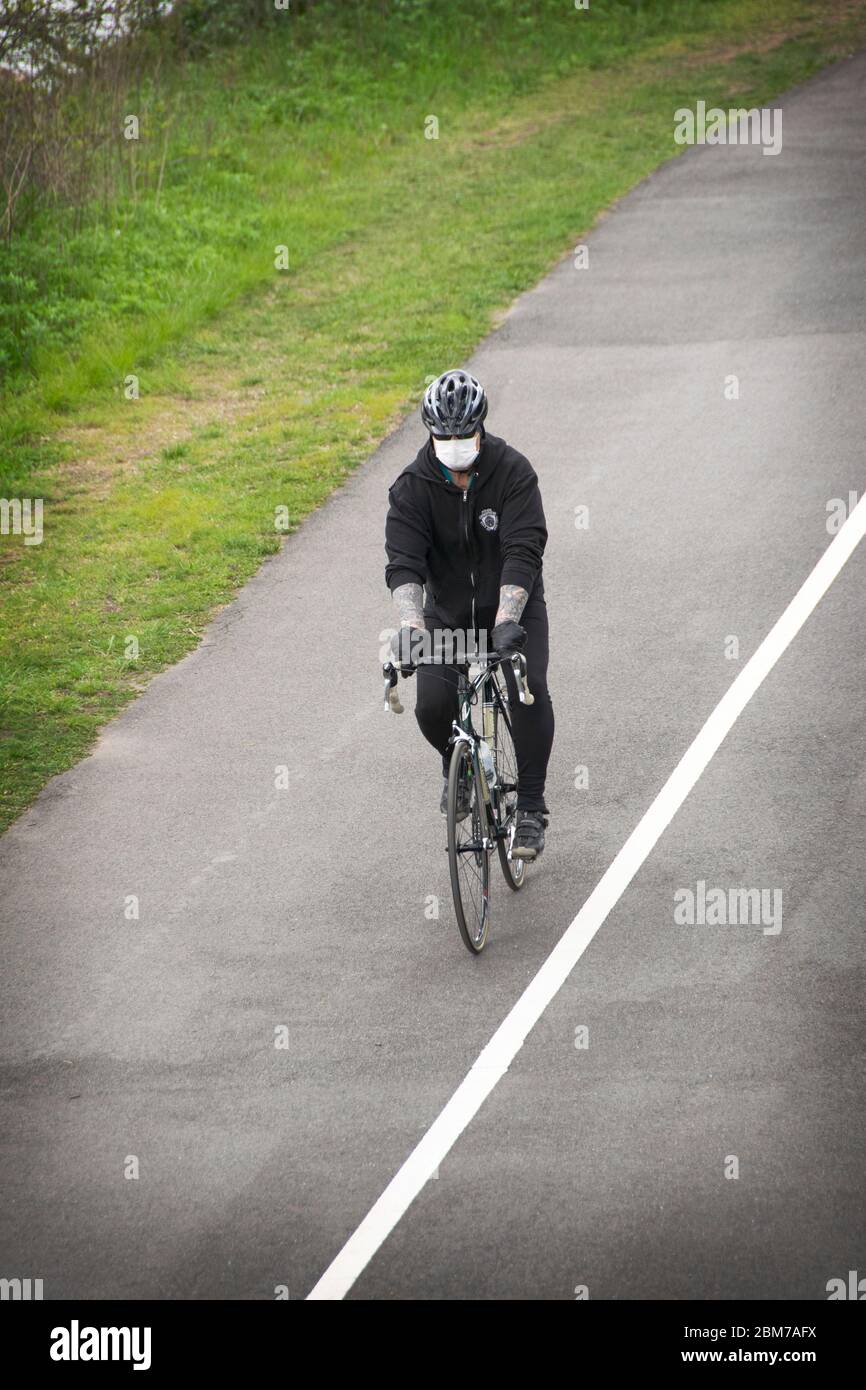 A man with tattoos biking wearing a surgical mask during the coronavirus plague. On the path near the Bayside Marina in Bayside, Queens, New York City Stock Photo