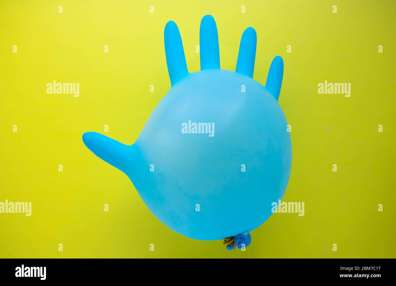 Flying blue rubber surgical glove in the form of a balloon on a yellow