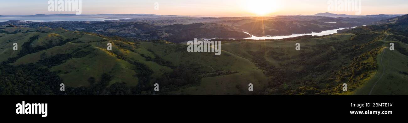 Sunlight illuminates the green hills of the East Bay. West of these tranquil hills and valleys is the densely populated area of San Francisco Bay. Stock Photo