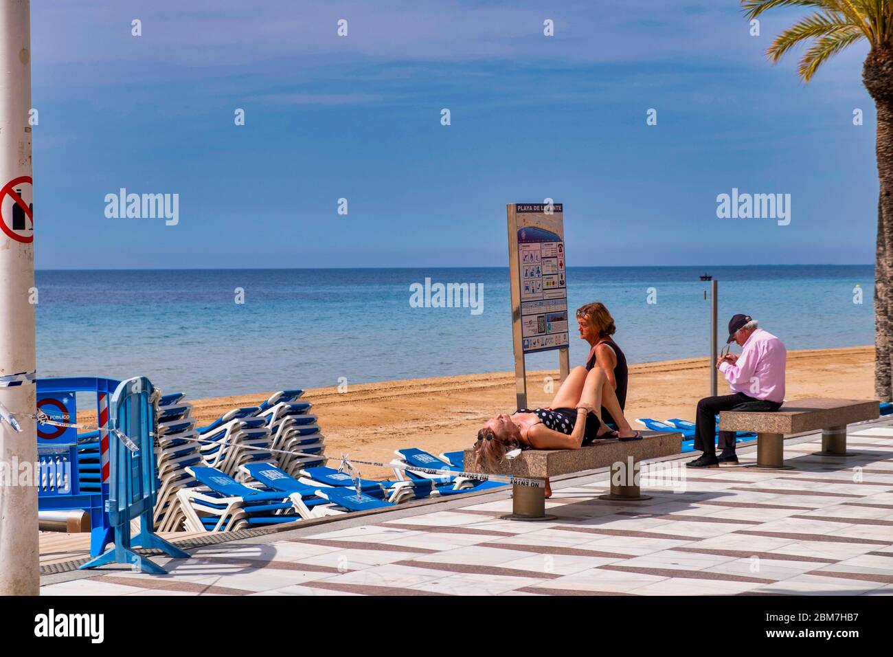 Benidorm, Alicante Spain, 4.5.2020, corona crisis: three people sit and lie on stone benches on the promenade on the deserted Playa Levante beach Stock Photo