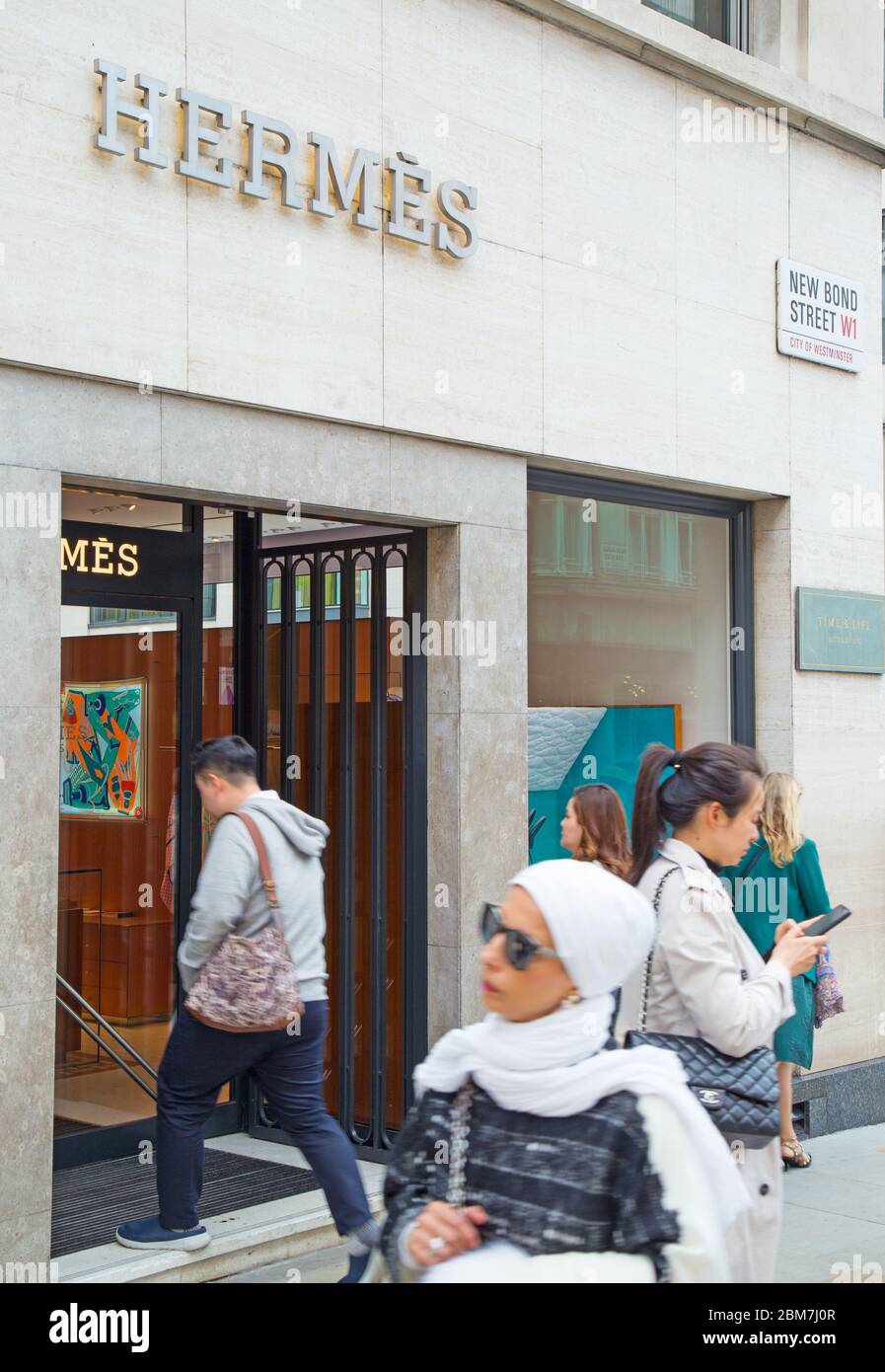 Smart-looking international shoppers, one of them Asian, walking past the Hermes luxury brand store on Bond Street in the West End of London, UK Stock Photo