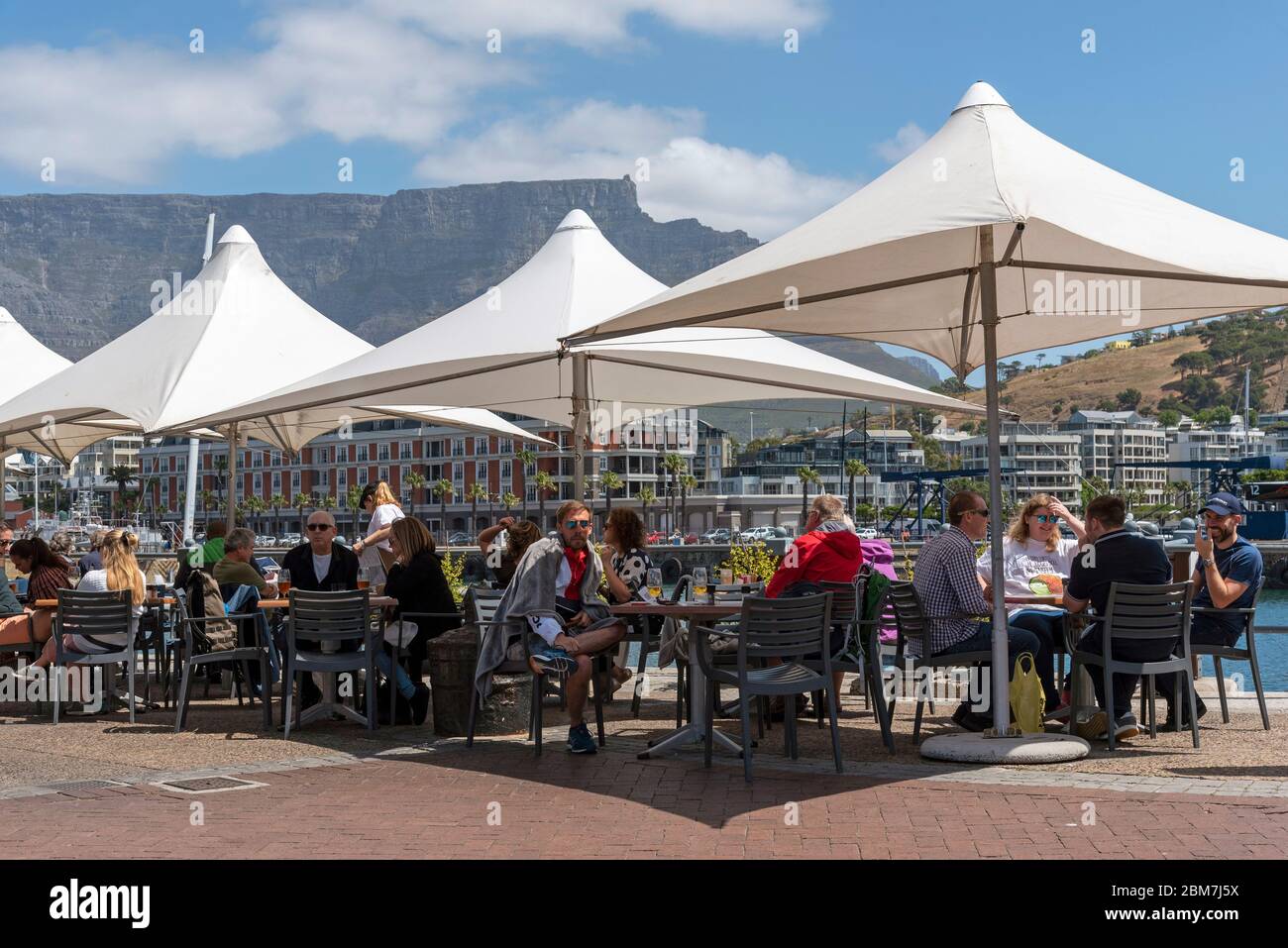 Cape Town, South Africa. 2019. People eating and drinking under umbrellas on the waterfront with