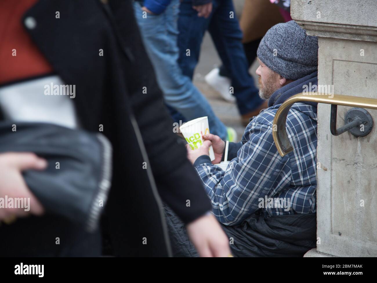 A homeless man sitting in a sleeping bag and holding a cup for